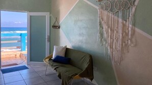 A room with a view of the ocean, a couch with a blanket, and a dreamcatcher on the wall. - Casita Linda (Arecibo)