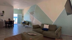 A living room with a sofa, ottoman, and a dining area with chairs and a table. - Casita Linda (Arecibo)