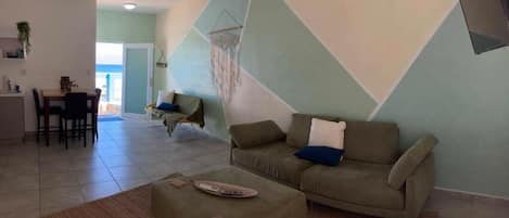 Un salon comprenant un canapé, un pouf et un coin repas avec des chaises et une table.