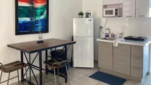 A compact kitchen with a refrigerator, microwave, and a small sink. There is a table with two chairs and a large abstract painting on the wall. - Casita Linda (Arecibo)