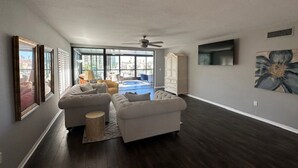 A spacious living room with dark hardwood floors, a large sectional sofa, and a view of a swimming pool through large windows. - 3-bedroom condo w/ water views in phenomenal Burnt Store Marina in Punta Gorda
 (Punta Gorda)