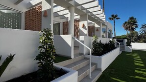 A modern building with a white exterior, a covered outdoor area with steps, and a well-maintained lawn. - Elegante Casa con Vistas al mar en la Playa #7 (Urbanova)