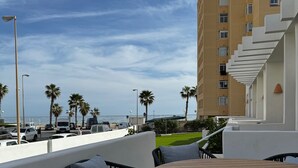 An outdoor seating area with a round wooden table and black wicker chairs, overlooking a parking lot and a building with a white staircase. - Elegante Casa con Vistas al mar en la Playa #7 (Urbanova)