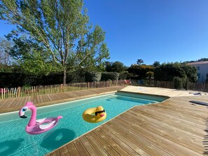 Une terrasse en bois entoure une piscine dans laquelle flottent deux bouées en forme de cygne gonflables.