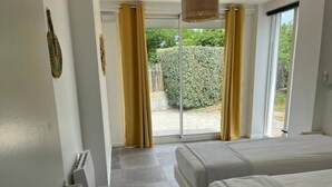Habitación de hotel con dos camas, una puerta corrediza de vidrio al exterior y vista a un jardín.