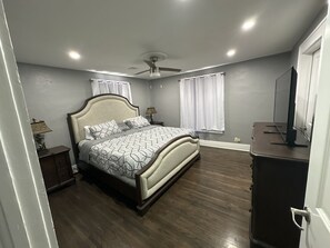 Une chambre à coucher comprenant un lit, un ventilateur de plafond, une table de chevet, une commode et un téléviseur.