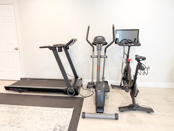 A home gym with a treadmill, elliptical, stationary bike, and a TV screen.