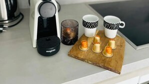 A kitchen counter with a coffee maker, two mugs, a glass, and a wooden board with candles. - New Studio in Belair with balcony (Luxembourg City)