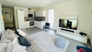 A modern living room with a sofa, a TV, a kitchen, and a dining area. - New Studio in Belair with balcony (Luxembourg City)