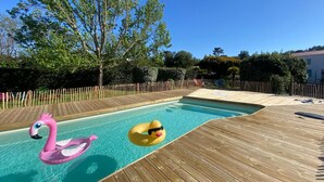 Une terrasse en bois entoure une piscine dans laquelle flottent deux bouées en forme de cygne gonflables.
