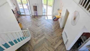 Une pièce spacieuse avec un parquet en point de Hongrie, un escalier blanc et un ventilateur mural.