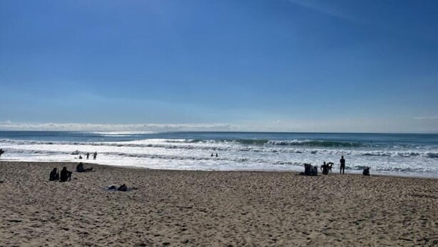 Une plage où l’on voit des gens assis et debout près de l’eau.