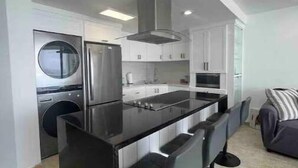 A modern kitchen with a central island, bar stools, built-in appliances, and a laundry area.