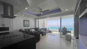A modern living room with a large window, a ceiling fan, and a kitchen area with a bar.