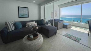 A modern living room with a dark-colored sofa, a round coffee table, and a large window offering a view of the ocean.