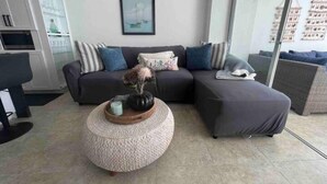 A modern living room with a grey sofa set, a round woven coffee table, and a framed picture on the wall.