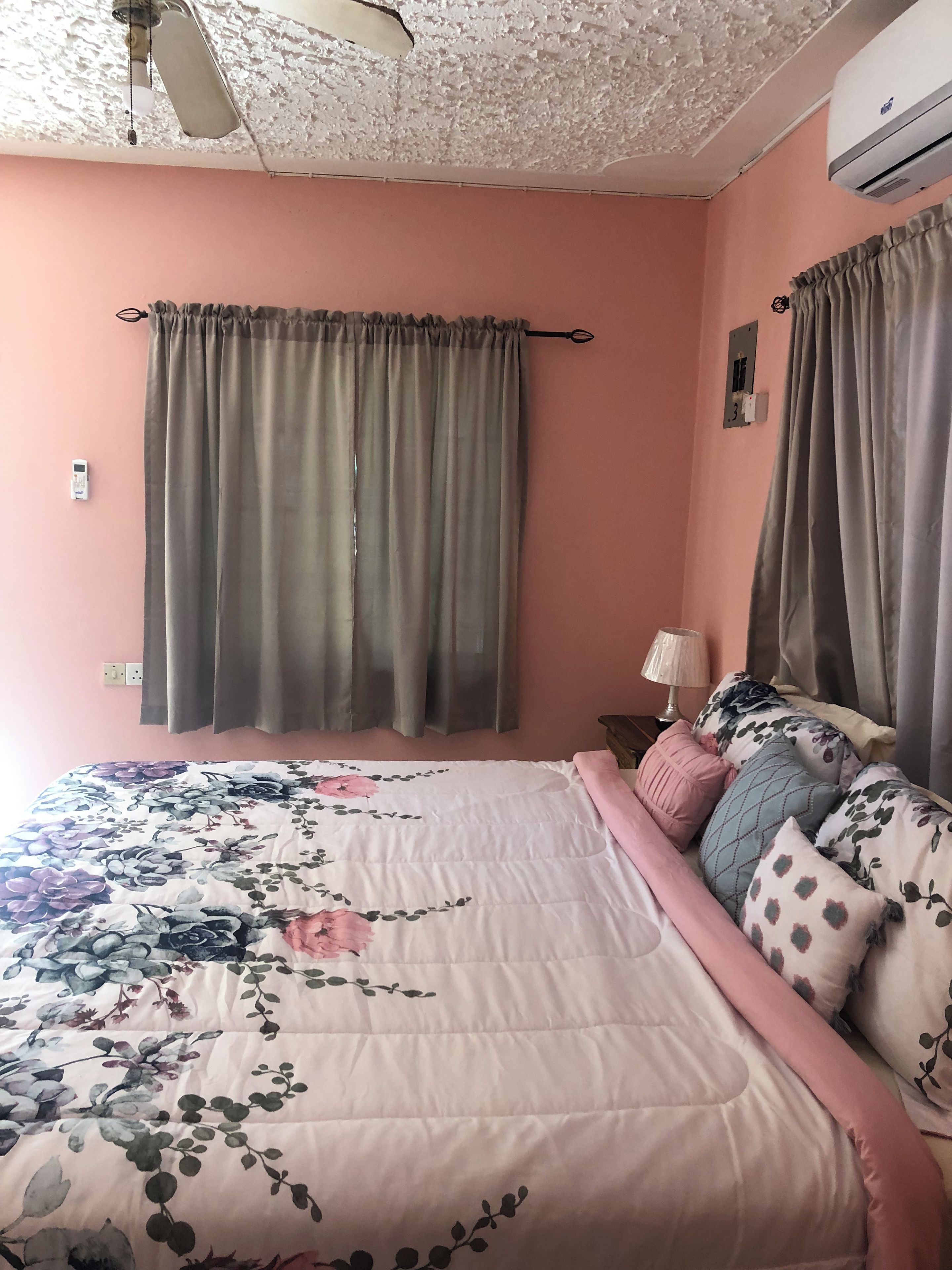 A bedroom with a floral bedspread, a ceiling fan, and two air conditioning units.
