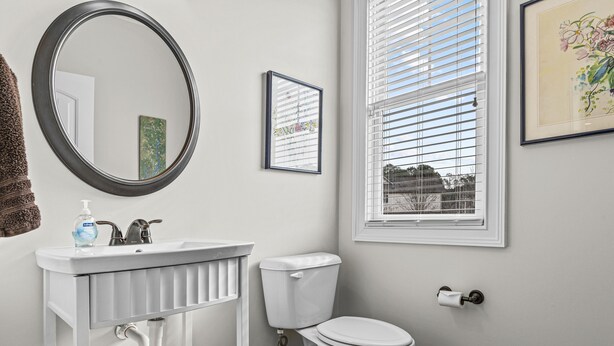 A bathroom with a white sink, toilet, and a window with blinds.