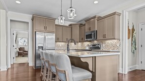 Ett modernt kök med träskåp, ett kylskåp i rostfritt stål, en mikrovågsugn och en stor köksö med barstolar.