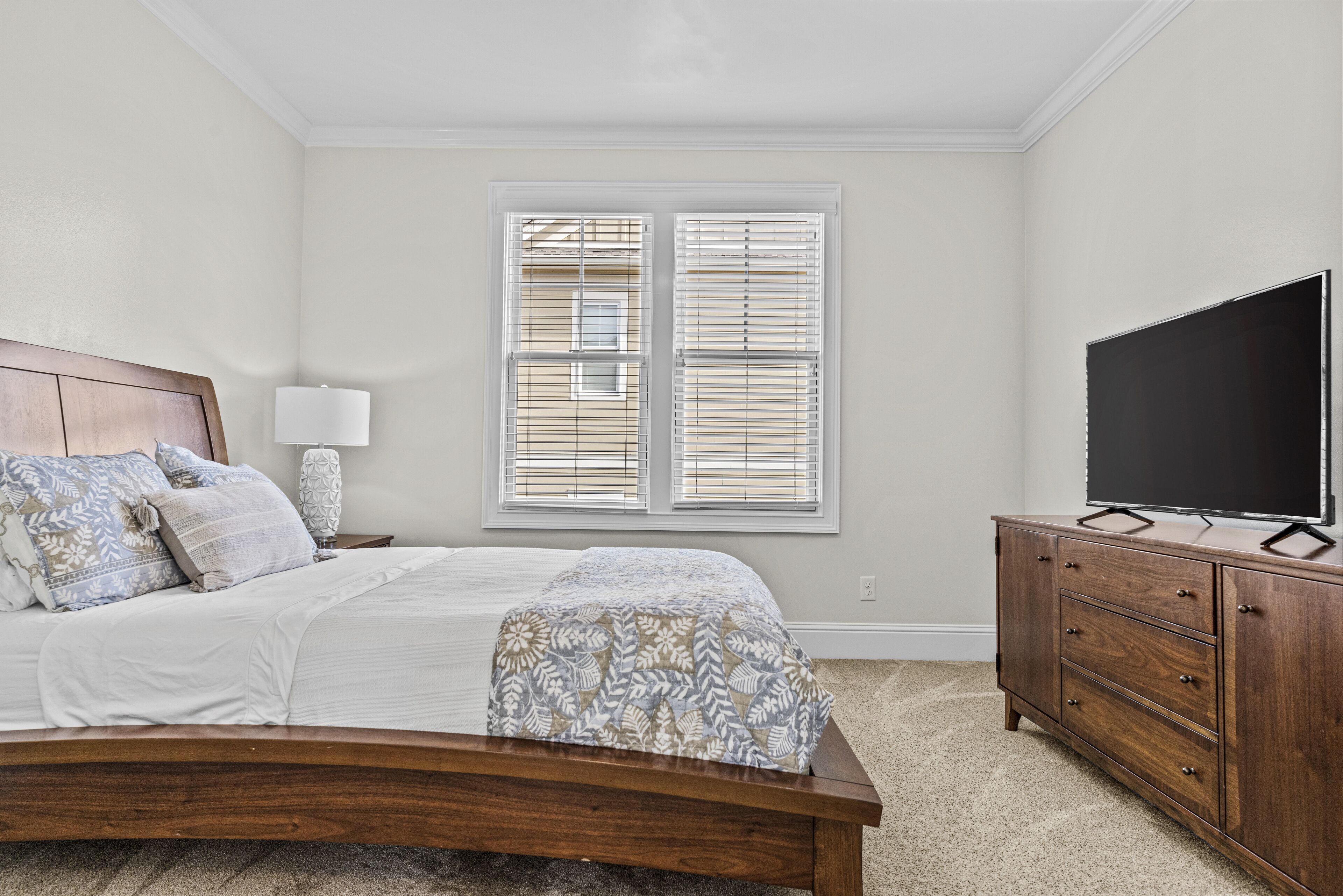 A bedroom with a wooden bed, a nightstand with a lamp, a dresser, and a TV.