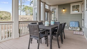 En inglasad veranda med ett bord och stolar, en välkomnande skylt och utsikt över det omgivande landskapet.