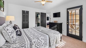 A bedroom with a bed, a ceiling fan, a TV, and a door leading to a balcony. - Mural House A: On The Trails > Private Hot Tub > Fire Pit > EV Charger (Bentonville)