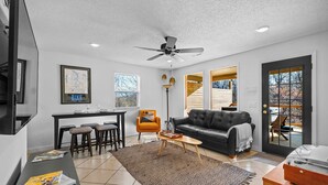 A modern living room with a black leather sofa, a dining area with a small table and chairs, and a kitchen area with a map on the wall. - Mural House A: On The Trails > Private Hot Tub > Fire Pit > EV Charger (Bentonville)