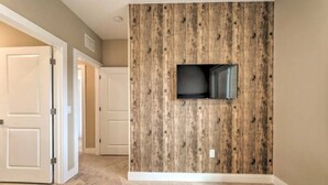 A hotel room with a wooden accent wall, a flat-screen TV mounted on it, and a carpeted floor.