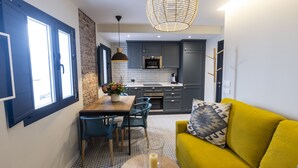 Une cuisine moderne avec des meubles gris, un coin repas avec une table et des chaises en bois, et un canapé jaune agrémenté d’un coussin à motifs.