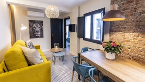 Un salon moderne avec un canapé jaune, une table à manger avec des chaises, un luminaire suspendu et un mur en briques.