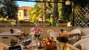 An outdoor café with tables, chairs, and a variety of food and drink items. - Hotel Villa Pina (Senigallia)