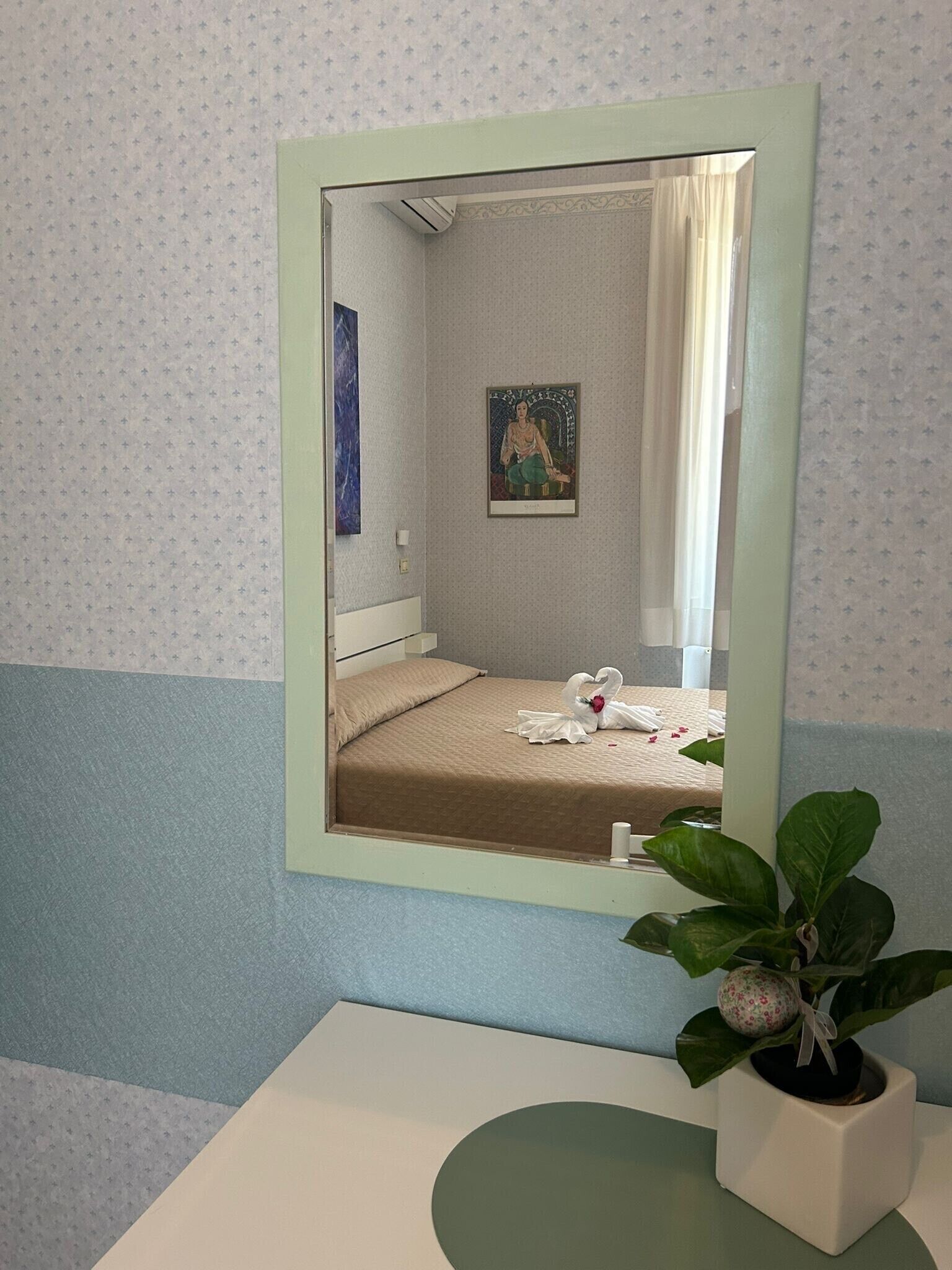 Una habitación de hotel con una cama, baño con lavamanos y un espejo que refleja la habitación.