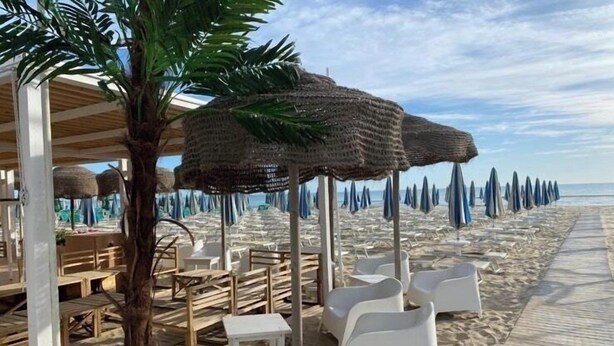 A beachside restaurant with outdoor seating, including white plastic chairs and tables, and thatched umbrellas. - Hotel Villa Pina (Senigallia)