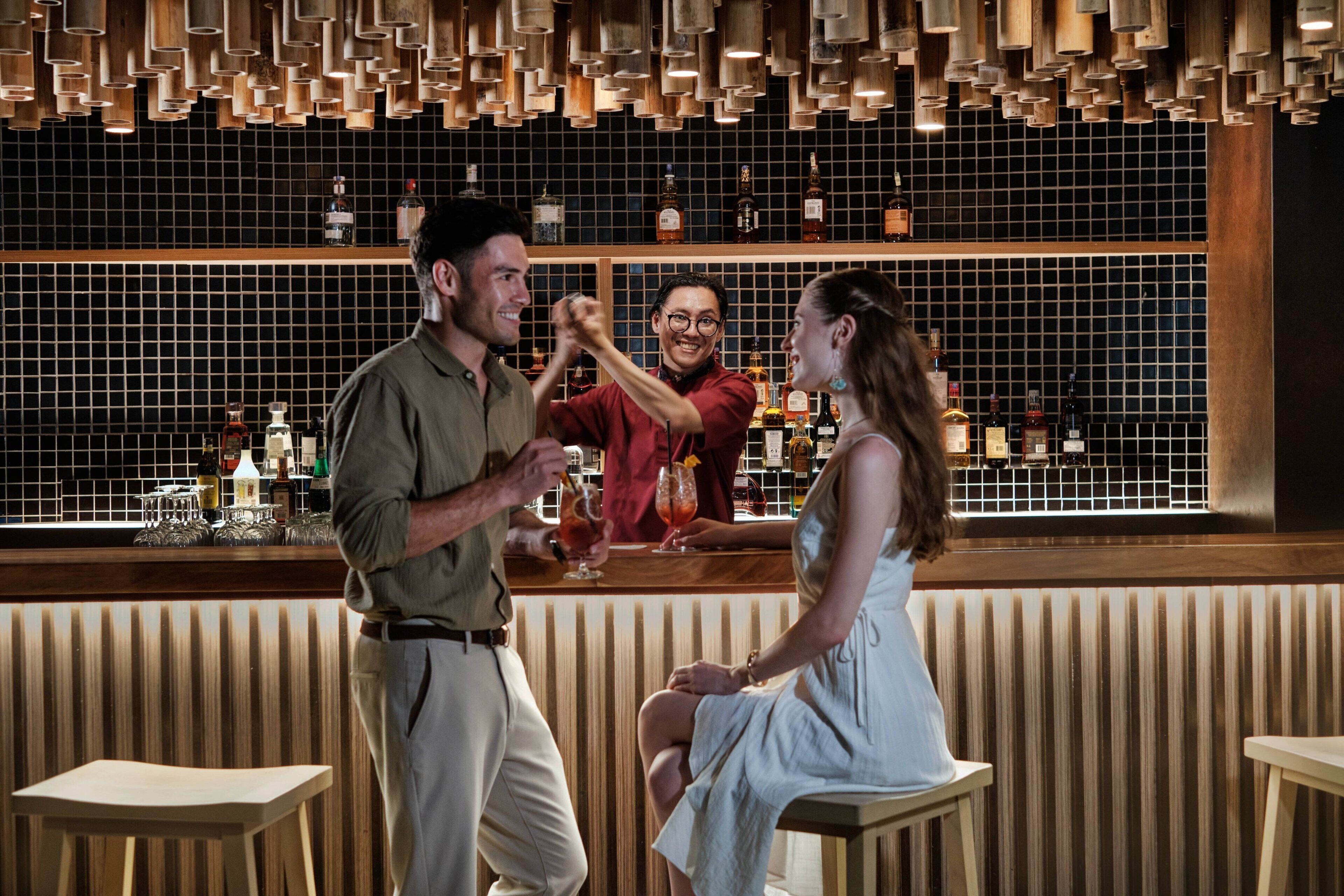 A bar area with wooden stools, a bar counter, and a tiled wall with bottles.