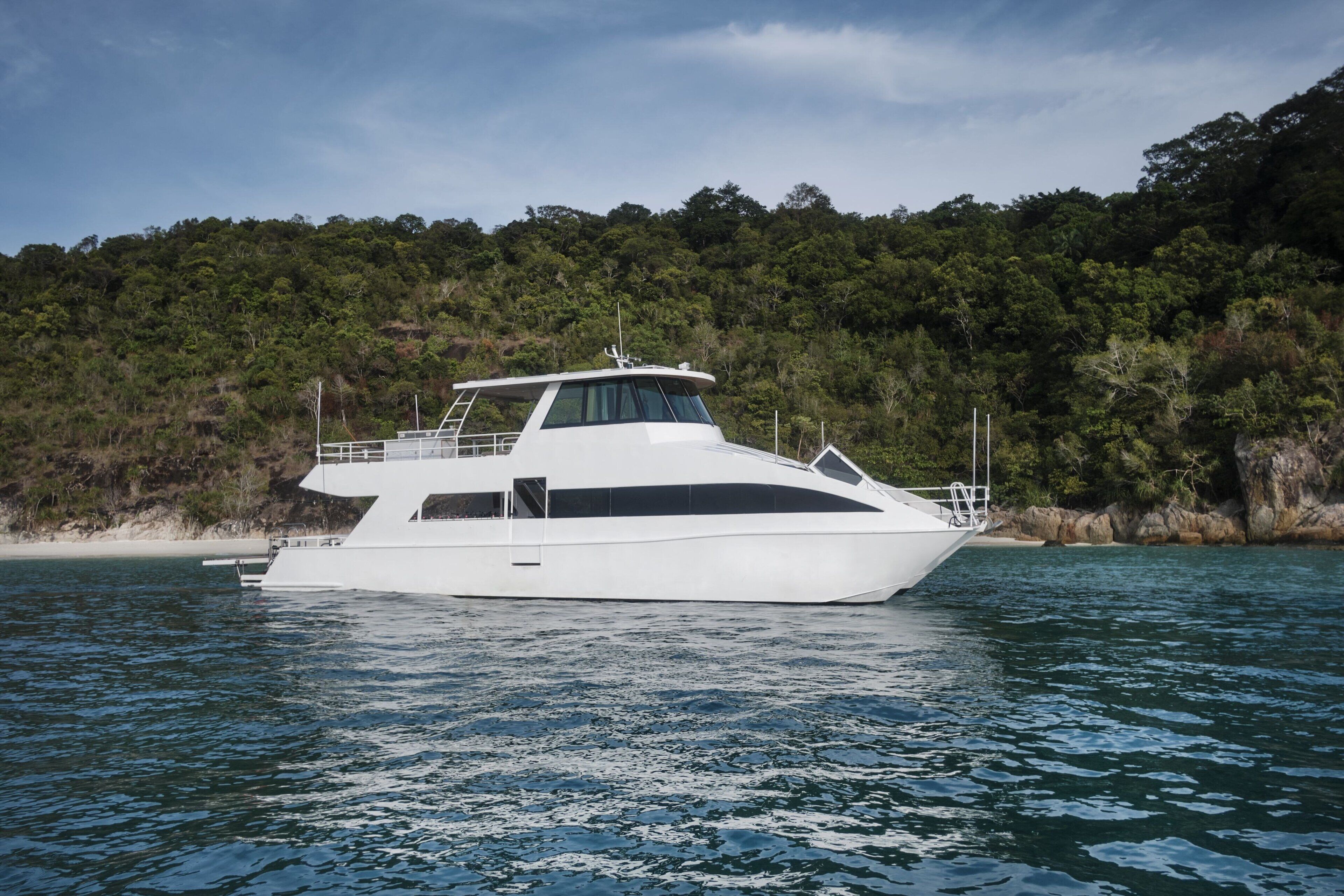 A white yacht docked near a forested coastline.