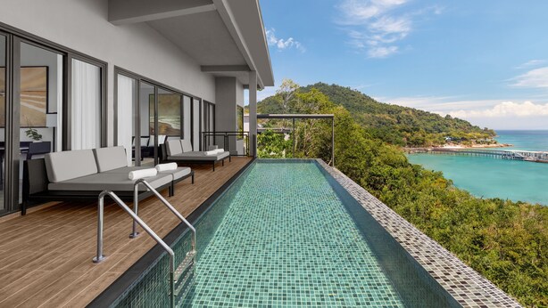 Ein moderner Außenpool mit Holzterrasse und Sitzbereich, mit Blick auf eine Küstenlandschaft mit Steg und üppiger Vegetation.