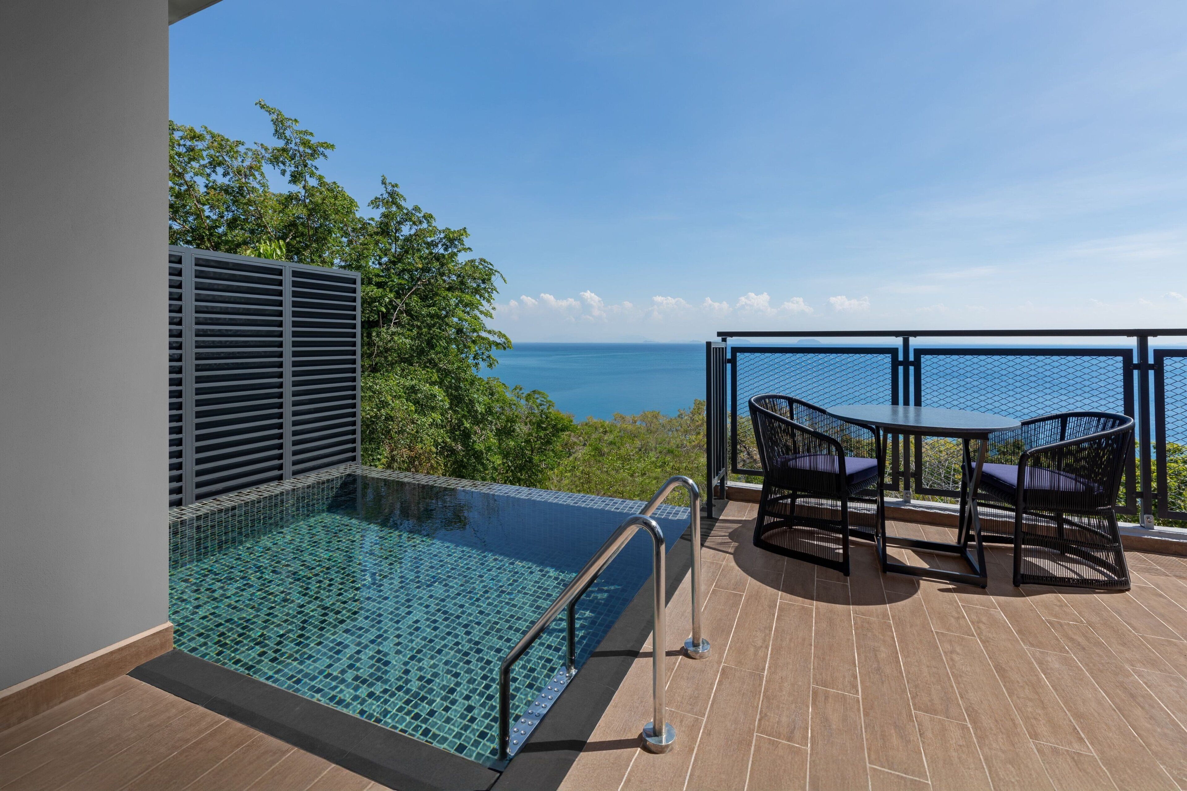 Une piscine sur le toit avec vue sur l’océan, une table avec des chaises et une rambarde.