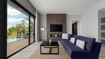 Een moderne woonkamer met een grote televisie, een donkerblauwe bank en uitzicht op een zwembad en groen.