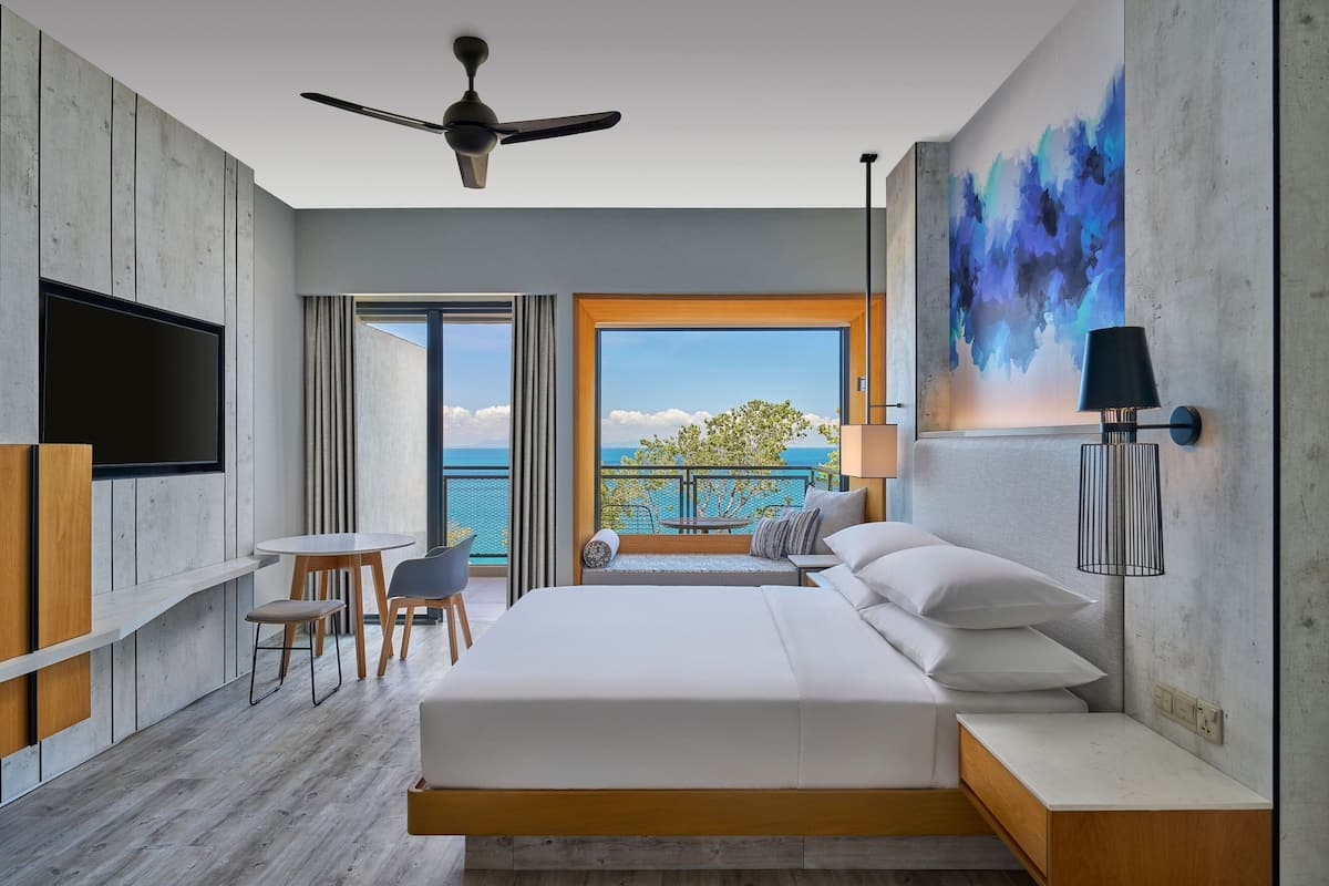 A modern hotel room with a large bed, a TV, a balcony with a view, and a ceiling fan.