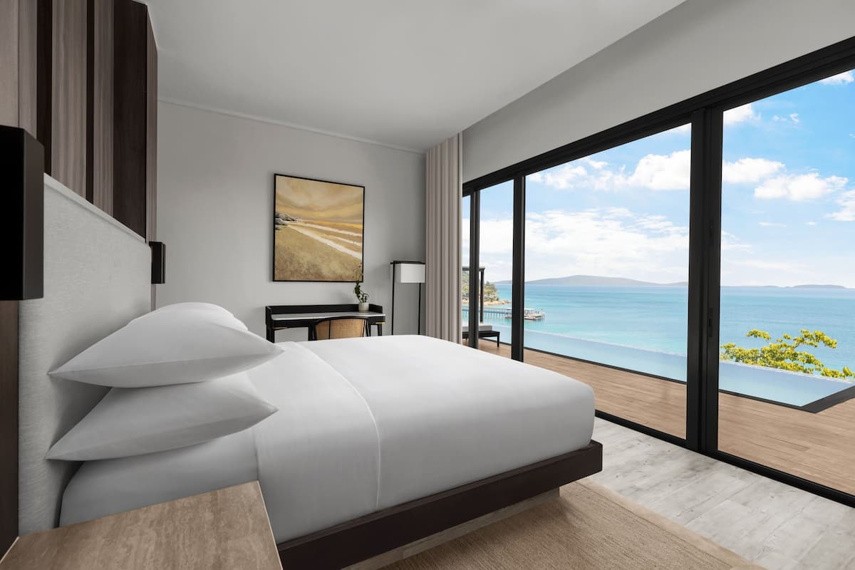 A modern hotel room with a large bed, a desk, and a view of the ocean.