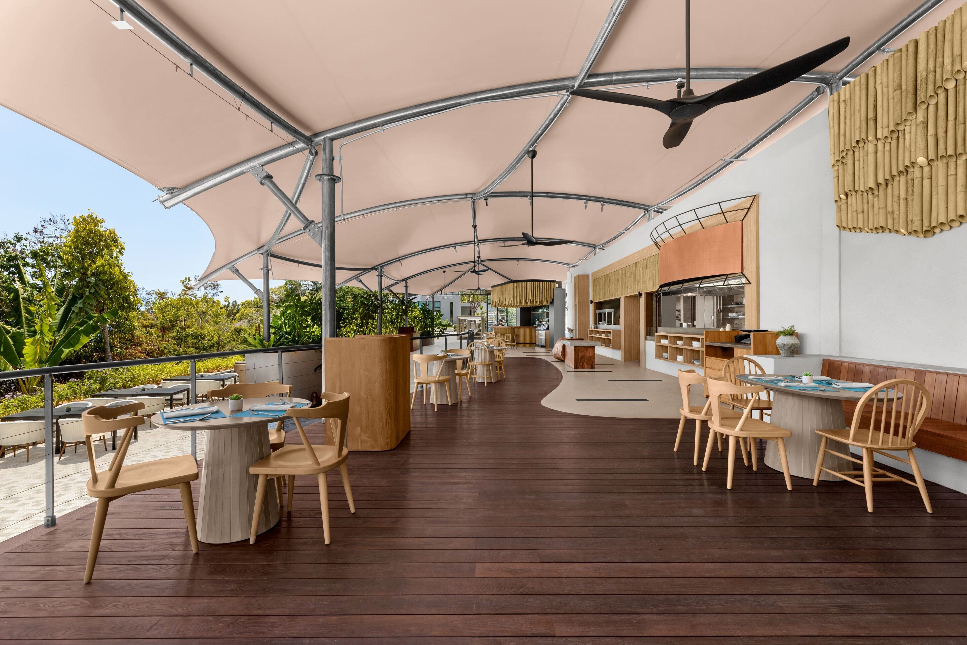 An outdoor dining area with wooden tables and chairs, a curved pathway, and a covered section with a ceiling fan.