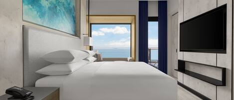 Une chambre d’hôtel moderne dotée d’un grand lit, d’un téléviseur à écran plat, d’un téléphone sur la table de chevet et offrant une vue sur la mer grâce à une grande fenêtre.