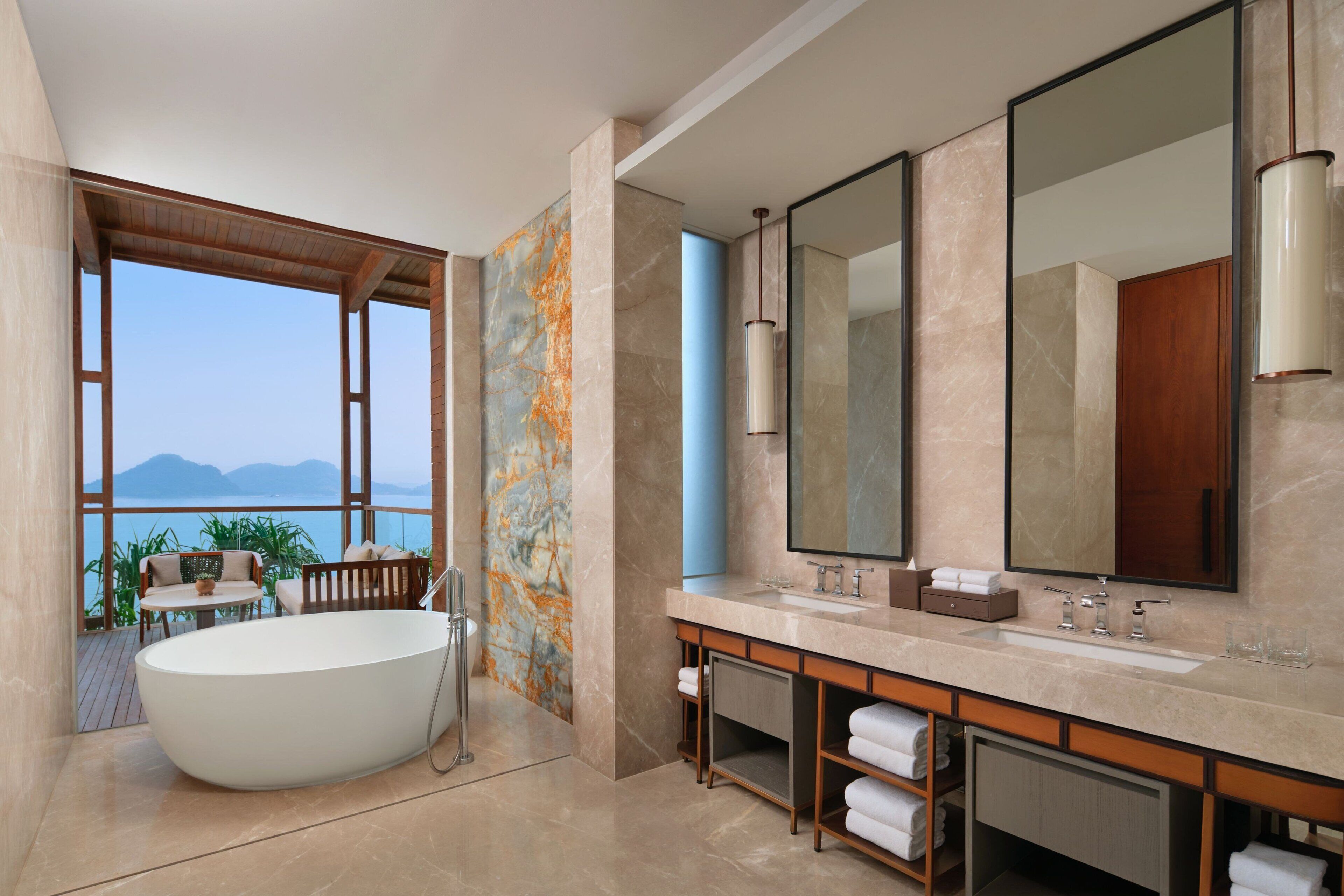 A modern bathroom with a large bathtub, a vanity with a mirror, and a view of the sea.