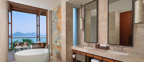 A modern bathroom with a large bathtub, a vanity with a mirror, and a view of the sea.