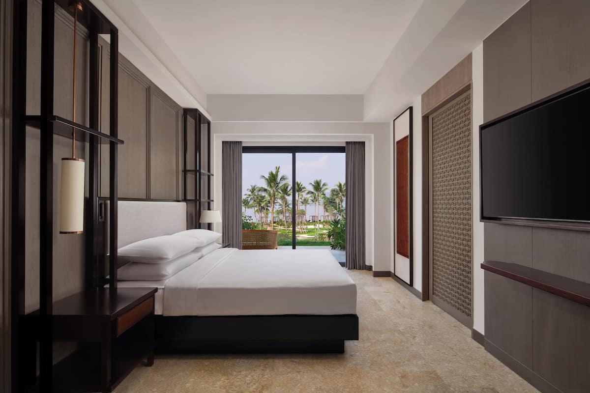 A hotel room with a large bed, a TV, and a view of palm trees.