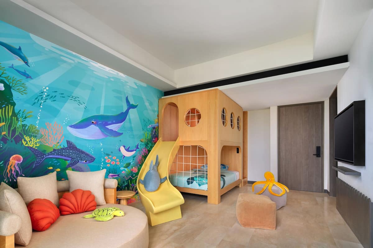 A children's playroom with a slide, a playhouse, and a mural of an underwater scene.
