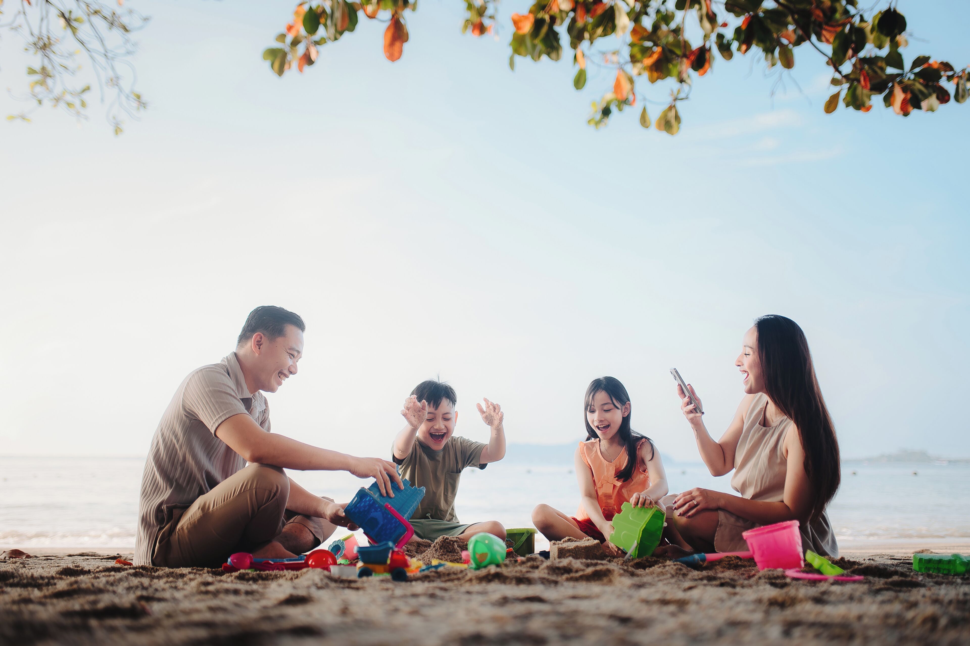 A group of people sitting on a sandy beach, playing with sand toys.