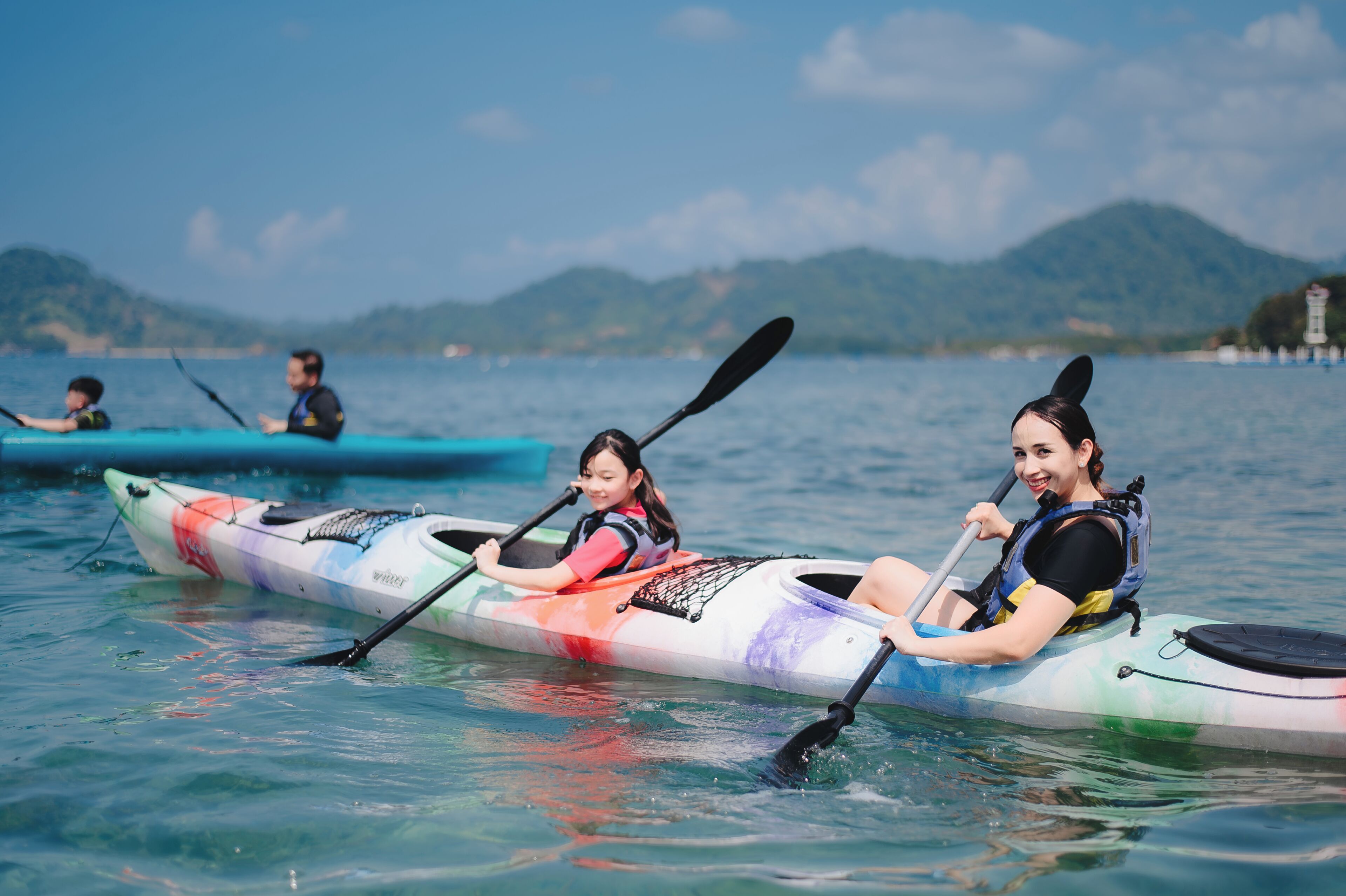 Un groupe de personnes pratiquant le kayak sur une étendue d’eau calme, avec des montagnes en arrière-plan.