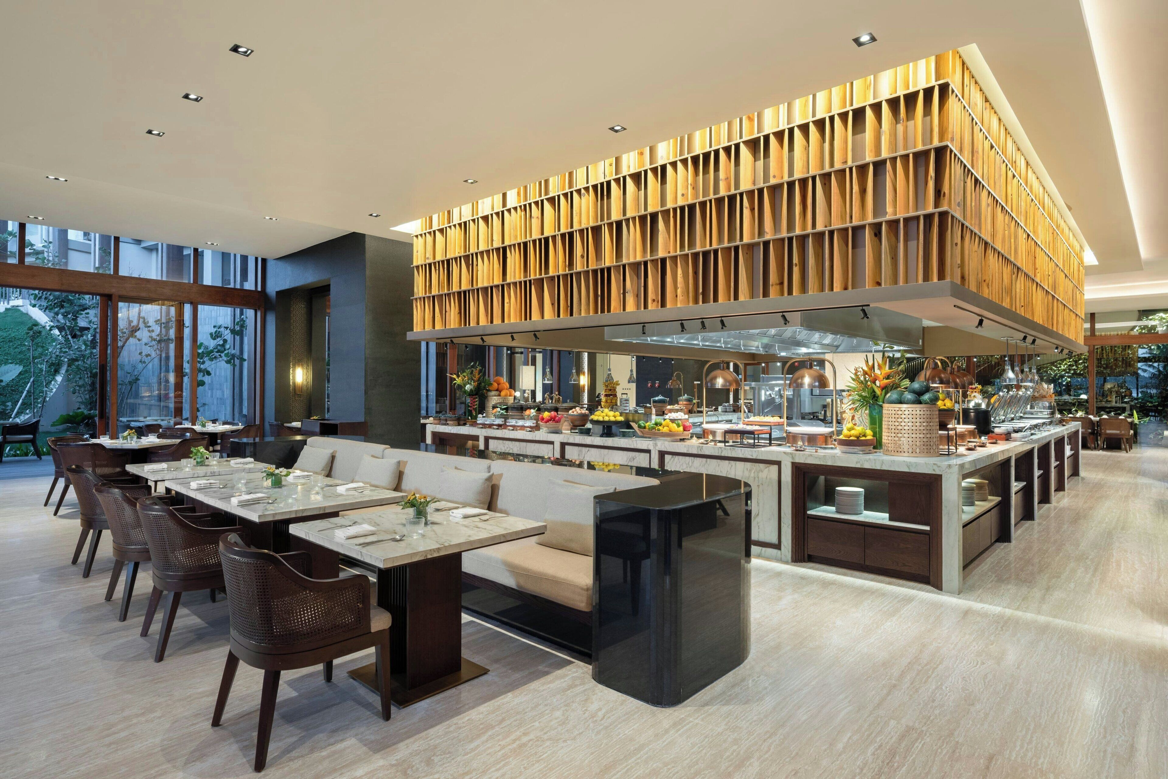 Un restaurant moderne doté d’un îlot central, d’un mur revêtu de panneaux en bois et offrant différents types de sièges.