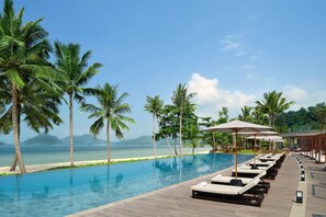 A poolside area with lounge chairs and umbrellas, palm trees, and a view of the sea. - Lampung Marriott Resort & Spa (Bandar Lampung)